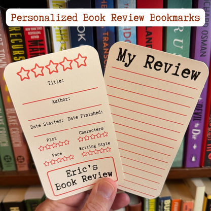 Two personalized book review bookmarks held in a hand in front of a bookshelf. One bookmark has a five-star rating section and the other has lined writing space with the heading 'My Review'.
